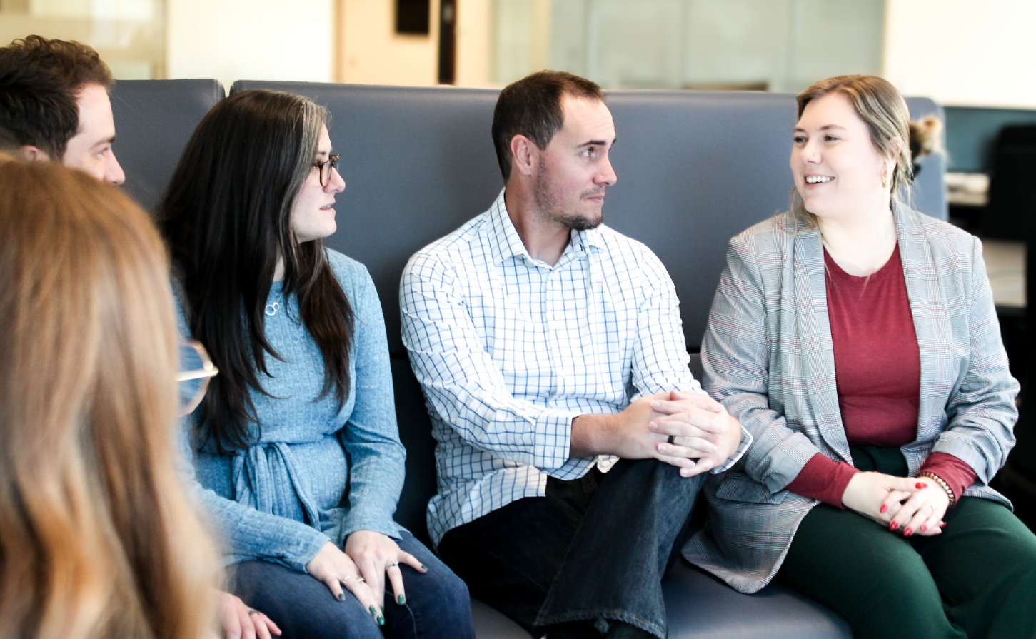 Five people sat in a cubicle at work having a meeting